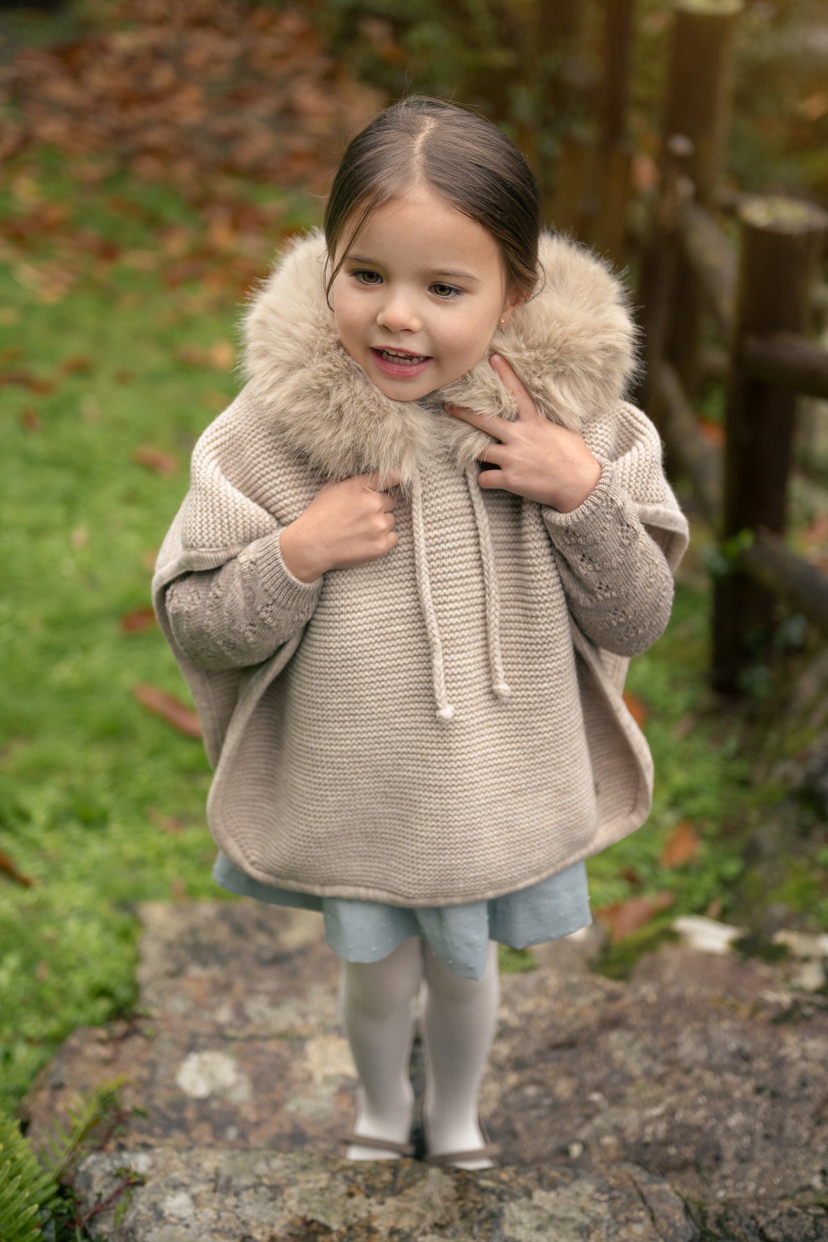 Poncho ESENCIAL color arena de Paz Rodríguez para niña, vista con modelo en exterior otoñal.